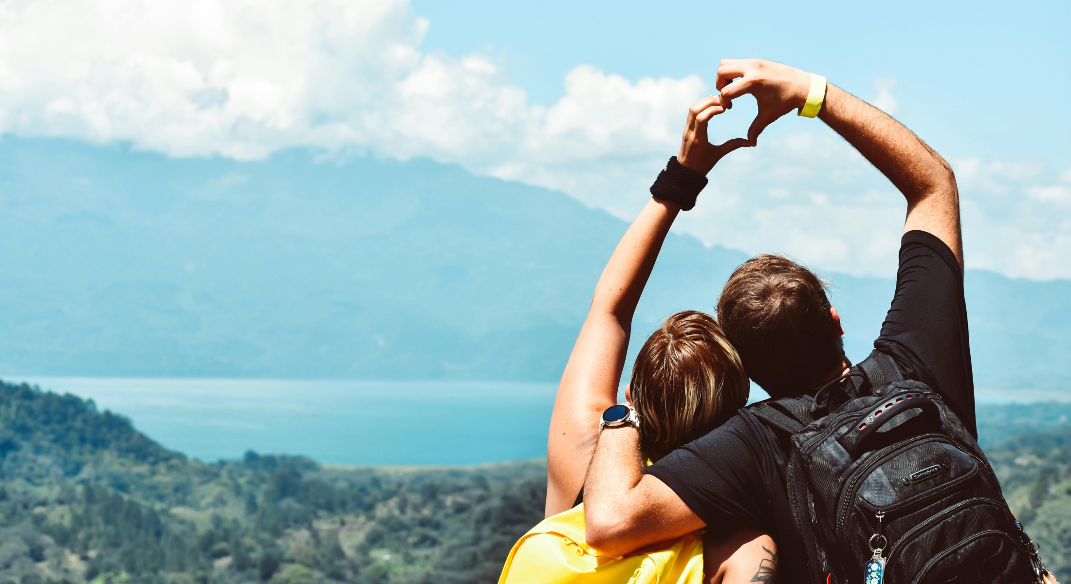 Coppia di escursionisti che forma un cuore con le mani davanti al lago e montagne