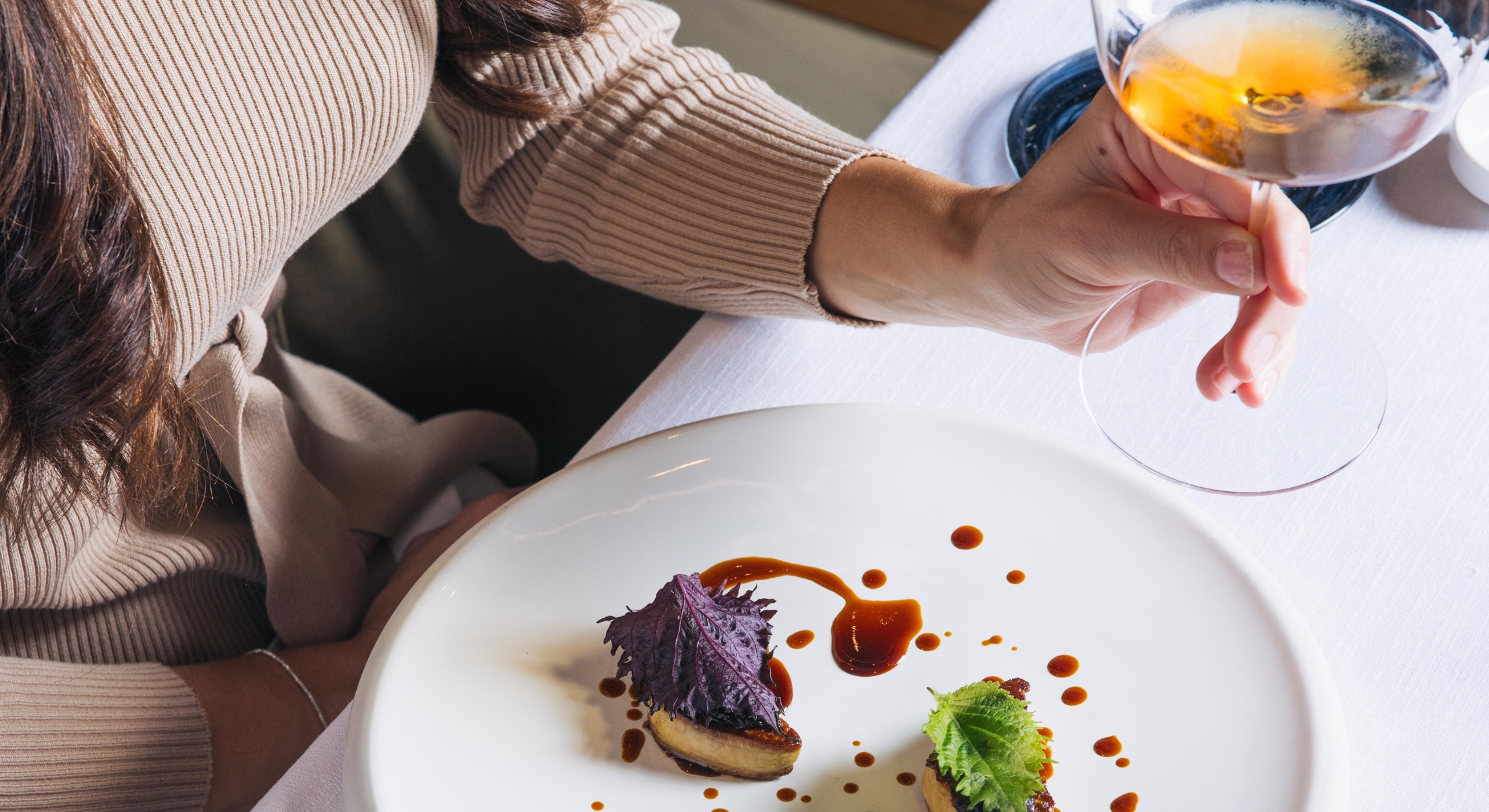 Donna a tavola con calice di vino bianco e piatto gourmet con presentazione raffinata