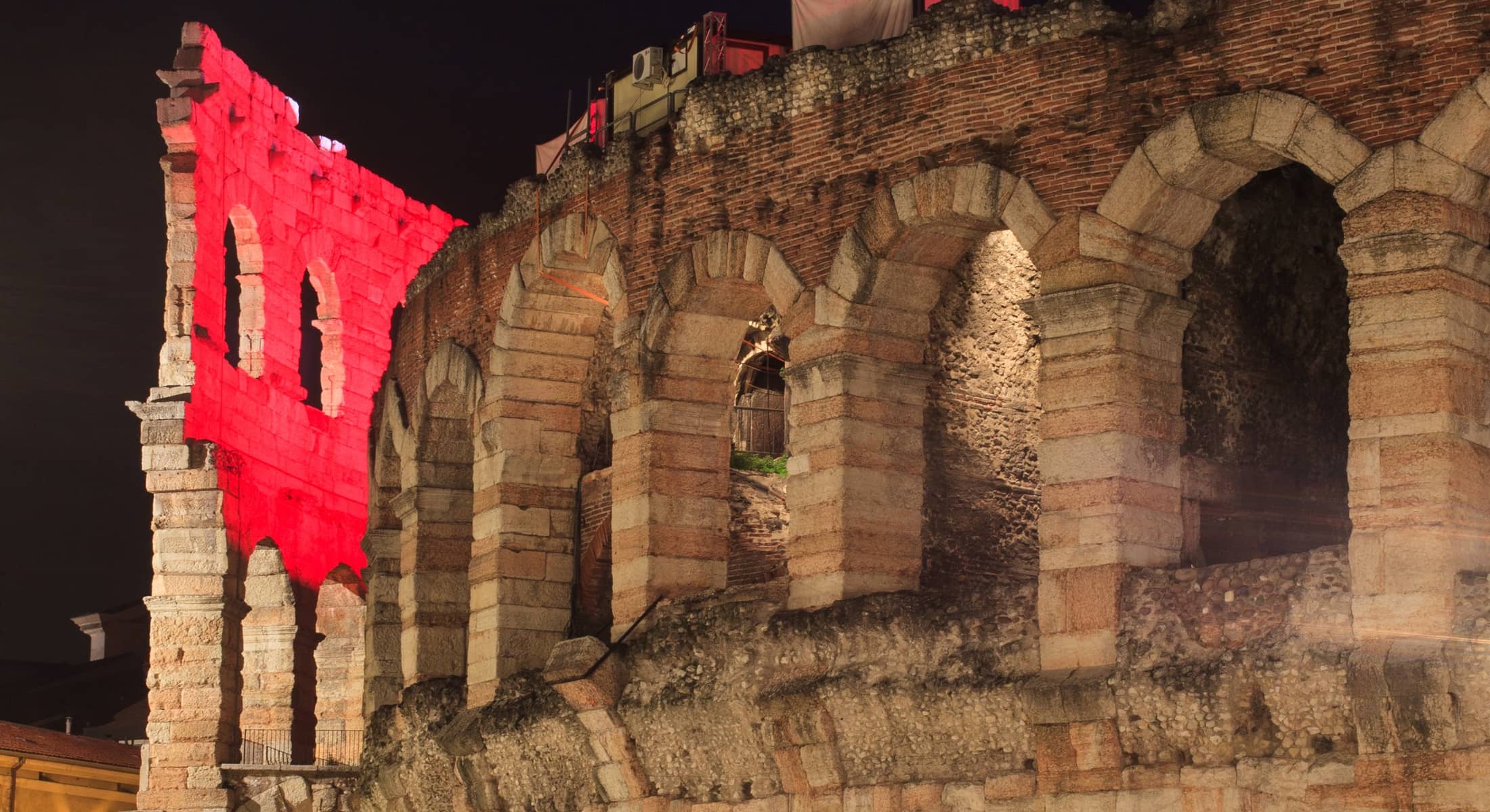Arena di Verona illuminata di rosso di notte, dettaglio delle arcate romane