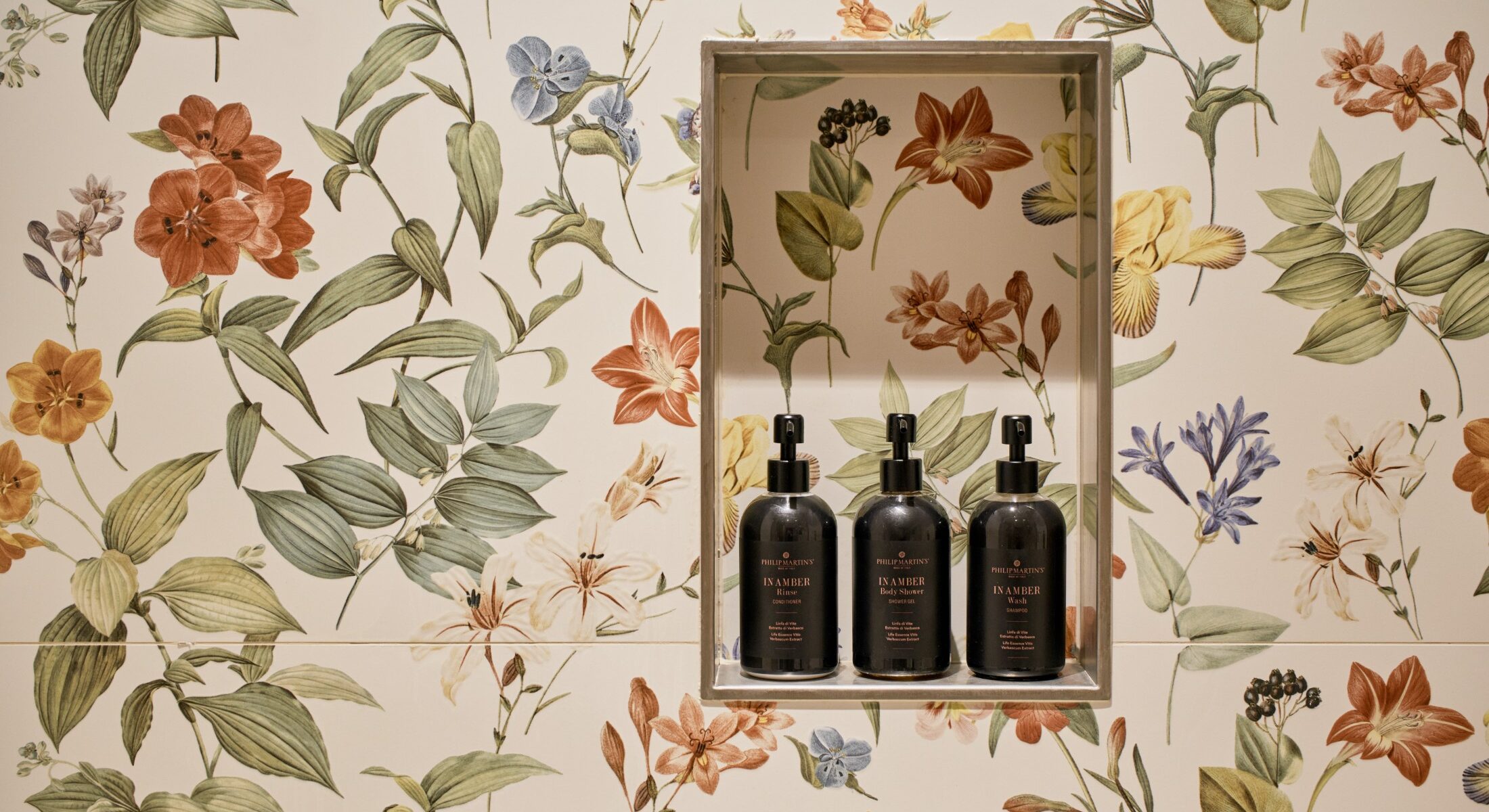 Dettaglio di parete floreale con set cortesia e flaconi neri – Homy Livia Verona