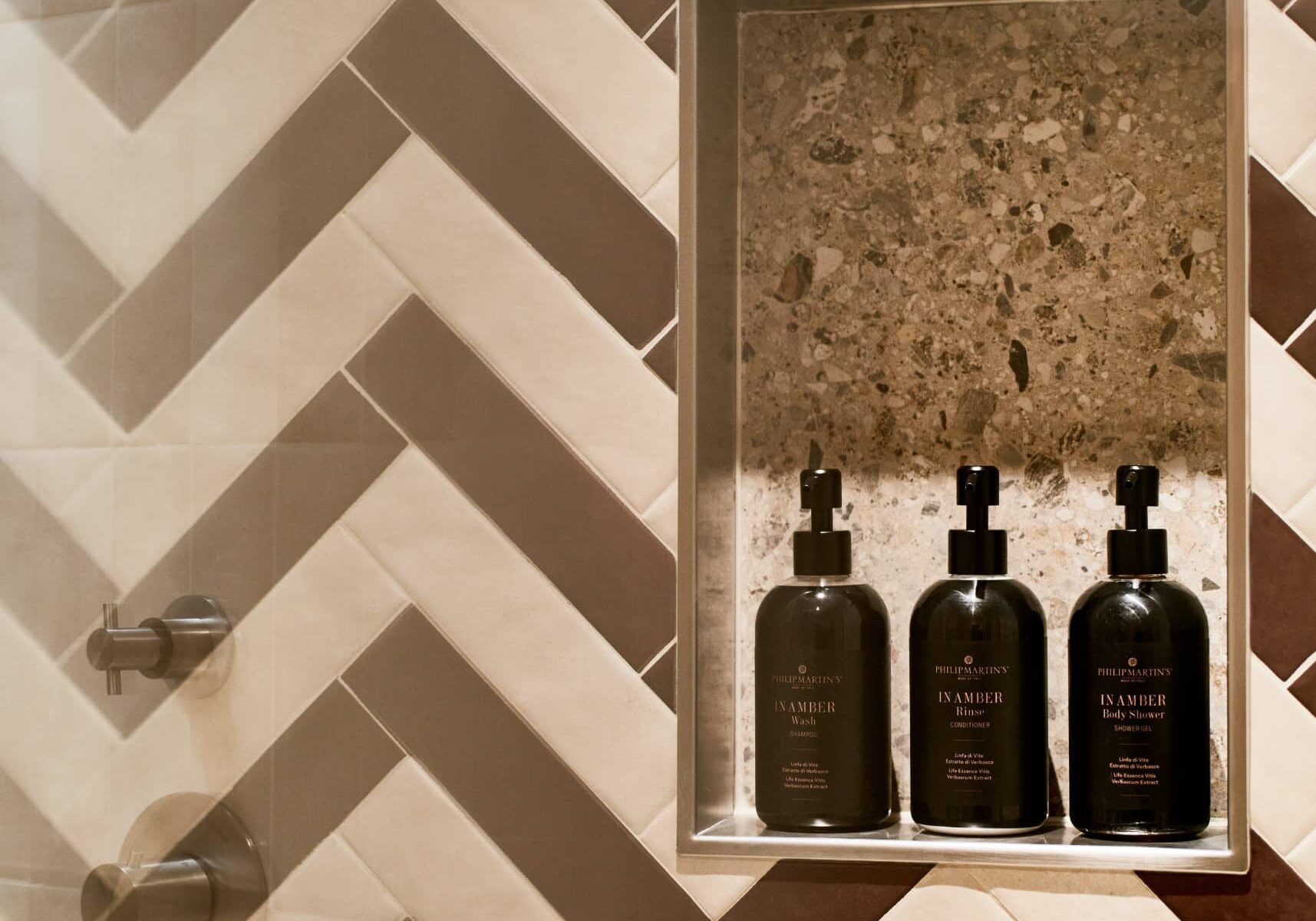 Parete doccia con piastrelle a spina di pesce e flaconi neri – Homy Livia Verona