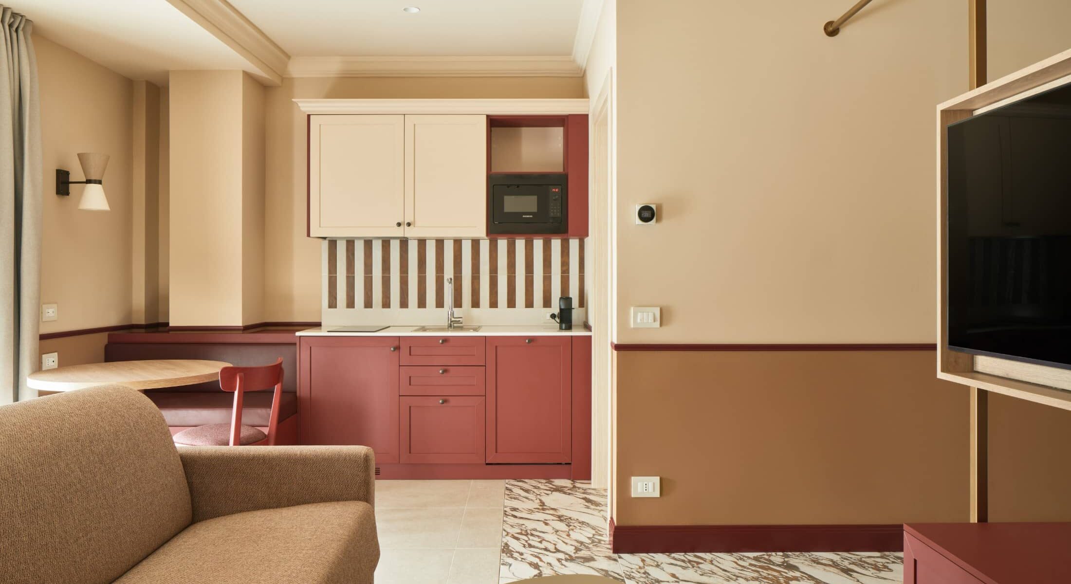 Soggiorno con divano color sabbia, cucicna e TV a parete – Homy Livia Verona