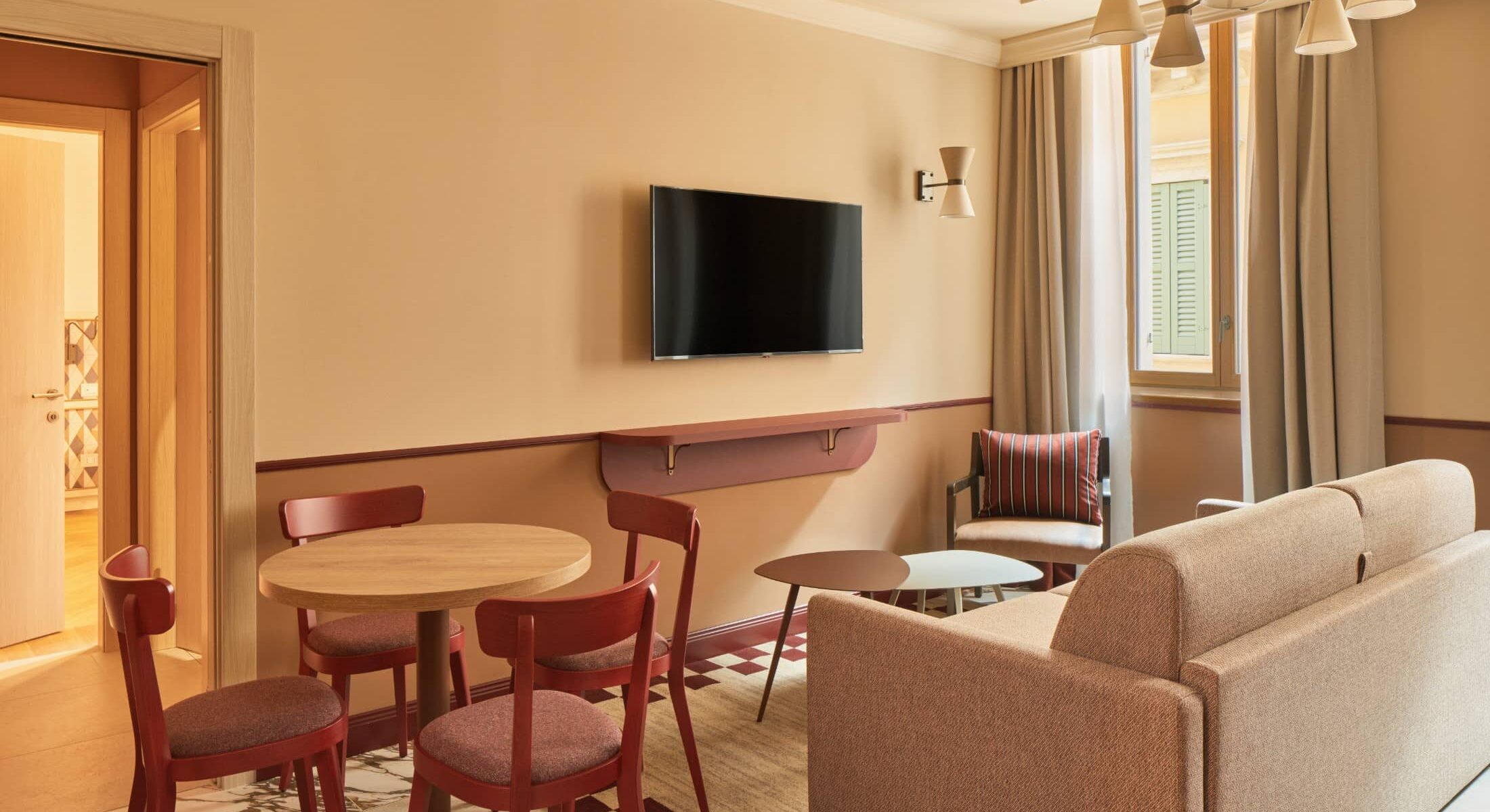 Soggiorno con divano color sabbia, tavolo da pranzo e TV a parete – Homy Livia Verona